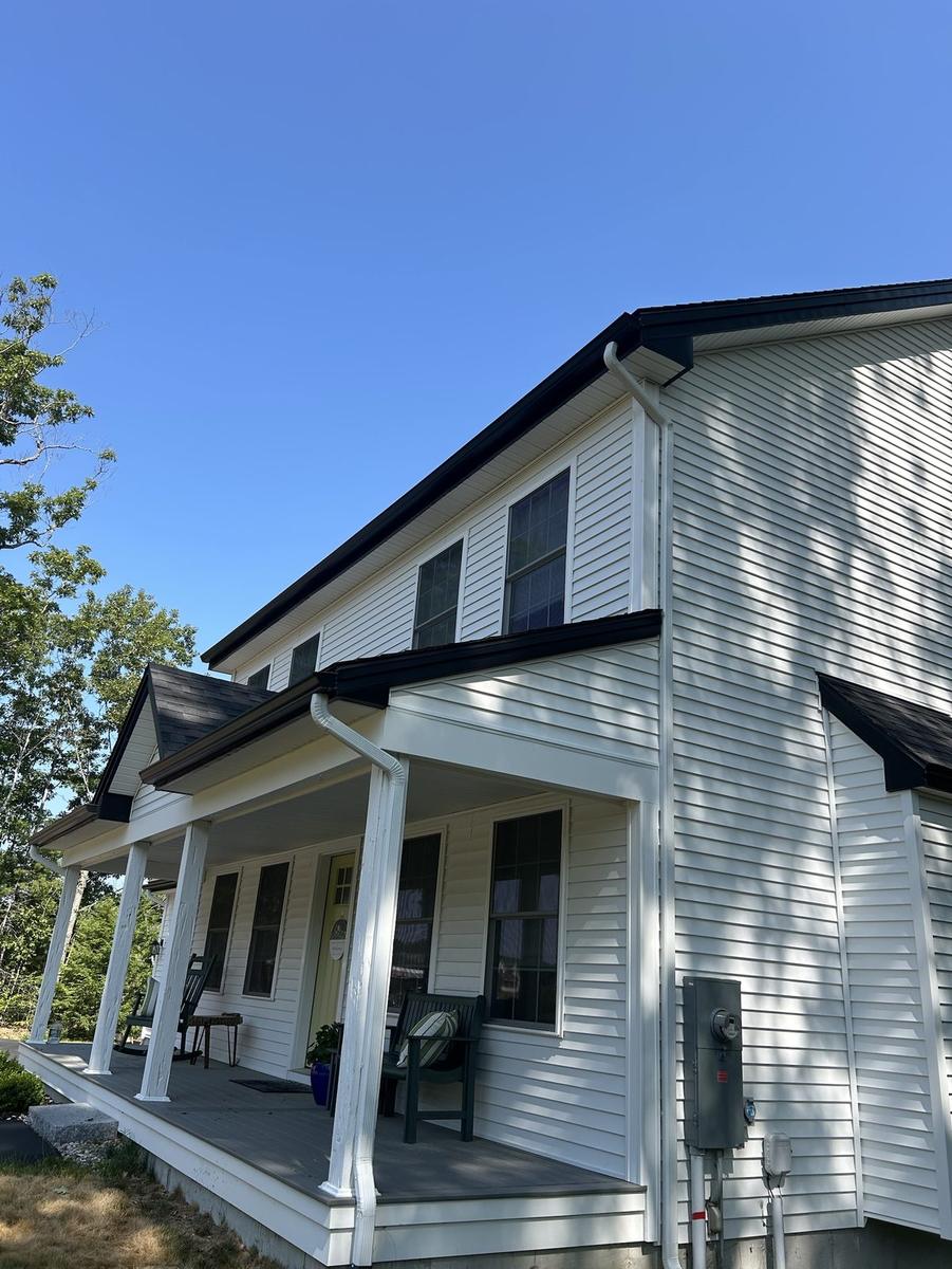 Dark seamless gutters and white downspouts on a Maine farmhouse
